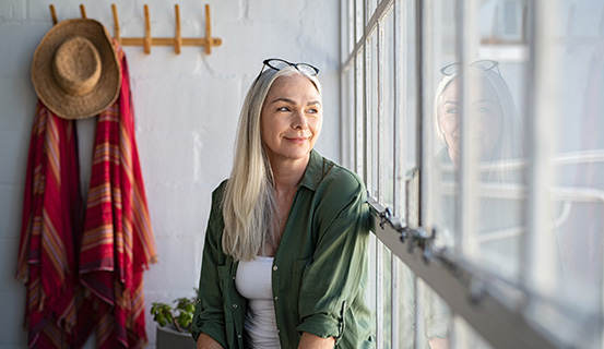 Frau sitzt lächelnd vor einem Fenster und schaut hinaus