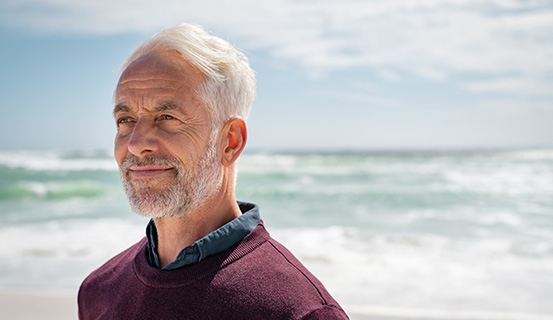 Älterer Mann steht am Meer und lächelt